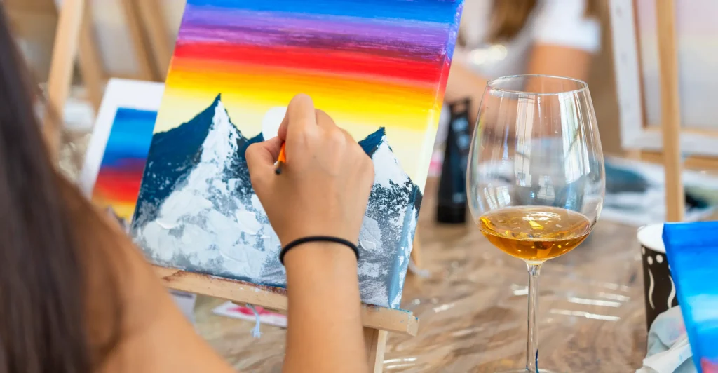 A woman painting with a glass of wine beside her